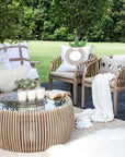 Tranquil outdoor lounge setting featuring the makena Chairs, a teak coffee table, and a cosy white-cushioned sofa styled with soft throws and textured cushions, set against a lush green garden backdrop