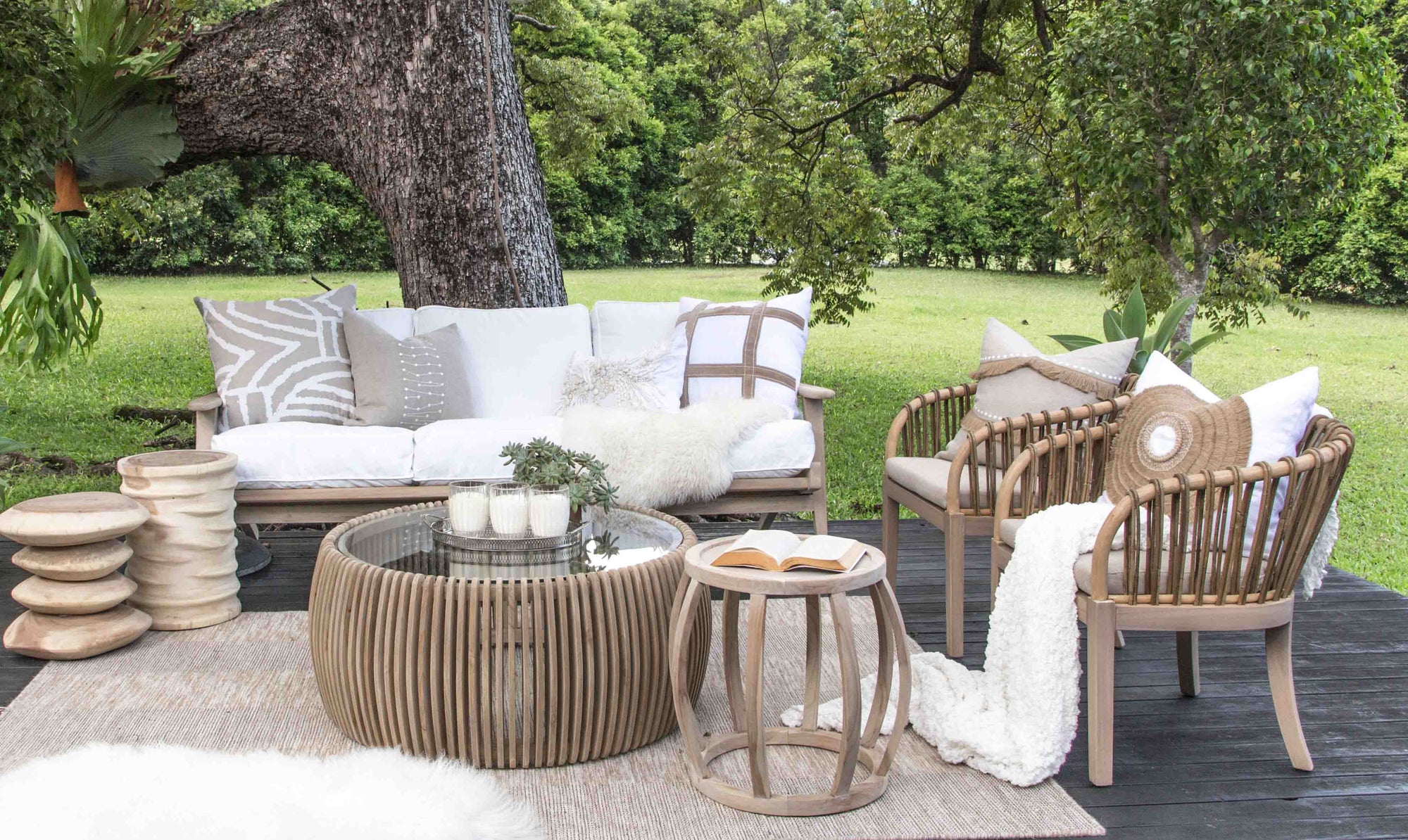 Tranquil outdoor lounge setting featuring the makena Chairs, a teak coffee table, and a cosy white-cushioned sofa styled with soft throws and textured cushions, set against a lush green garden backdrop