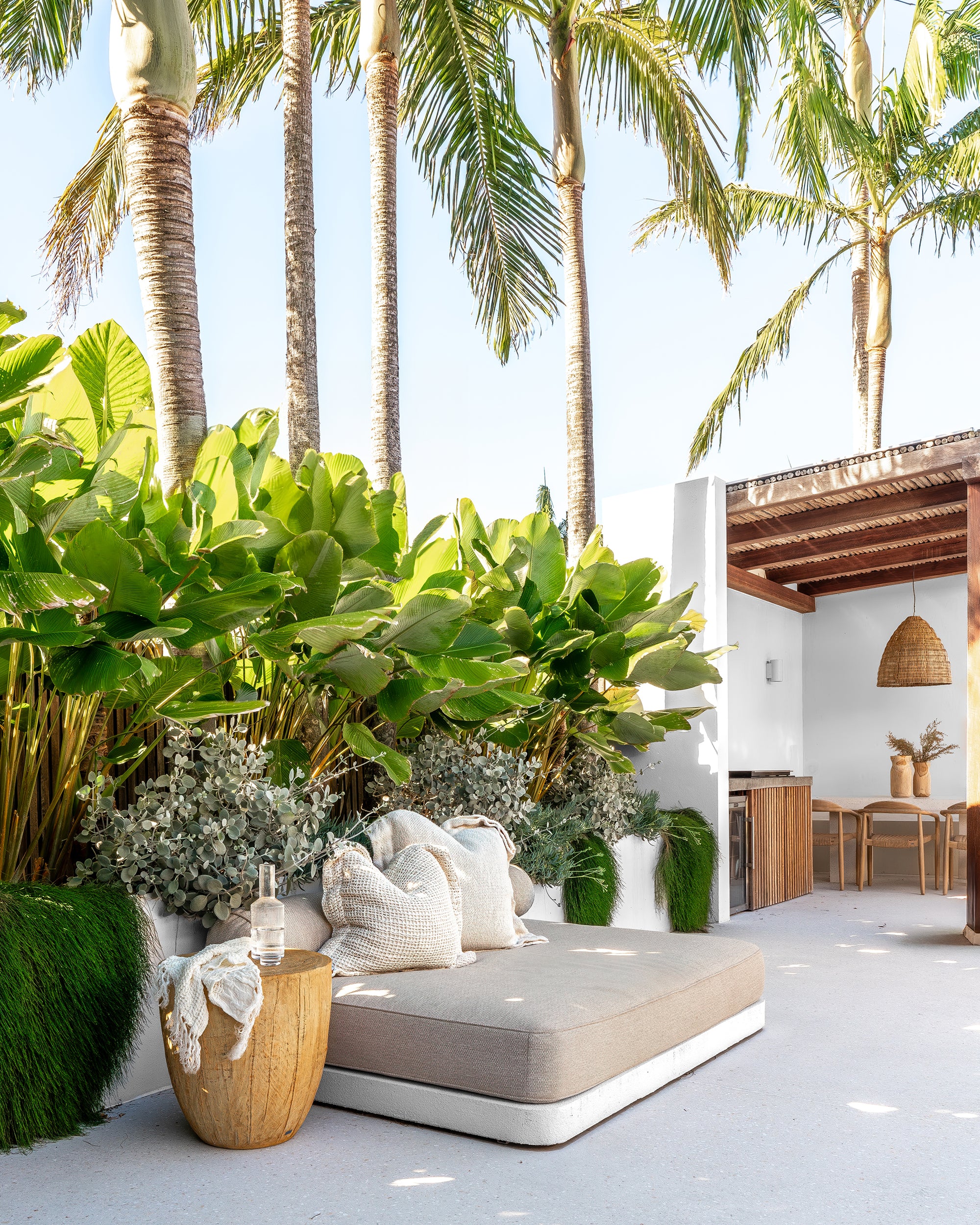 Outdoor daybed styled with soft neutral cushions, a magnesium oxide side table, and a throw, surrounded by lush tropical greenery for a serene, resort-style setting.