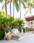Outdoor daybed styled with soft neutral cushions, a magnesium oxide side table, and a throw, surrounded by lush tropical greenery for a serene, resort-style setting.