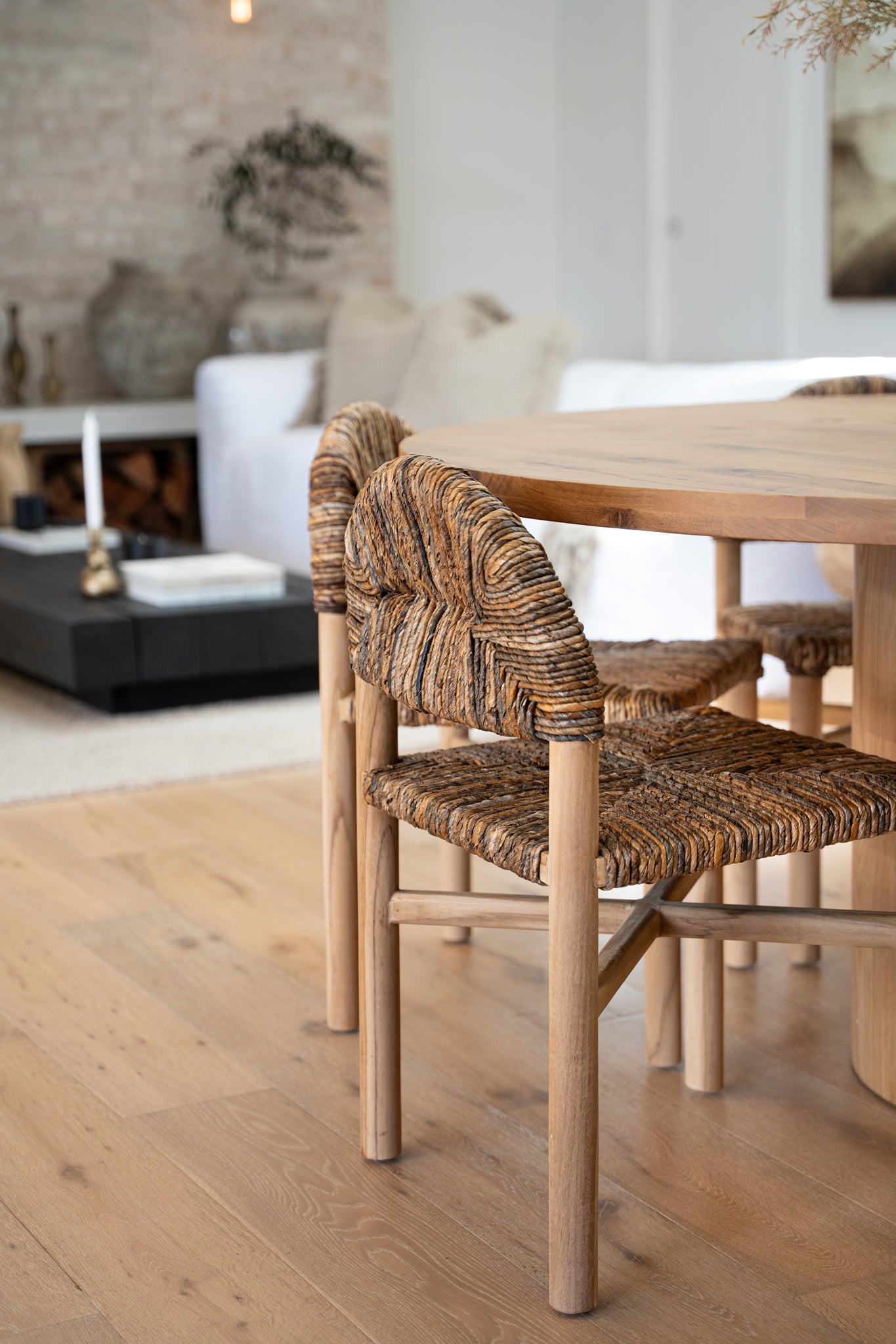 A close-up of a rattan and timber dining chair with an intricate handwoven seat and backrest, styled with a solid wood dining table in a neutral-toned living space. The warm, earthy textures enhance the organic modern aesthetic of the room