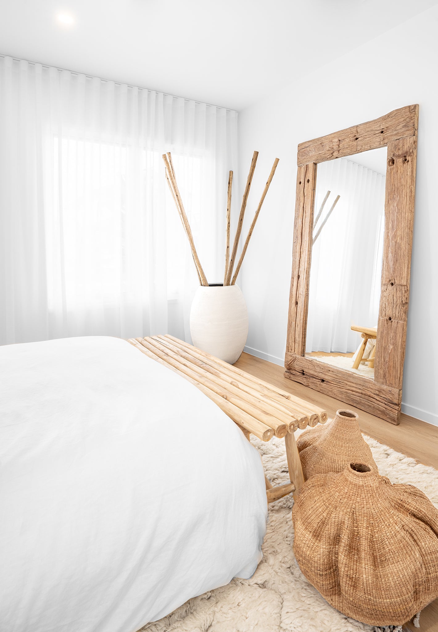 Rustic bedroom with natural rattan bench, woven baskets, and statement timber mirror, creating a serene and earthy aesthetic