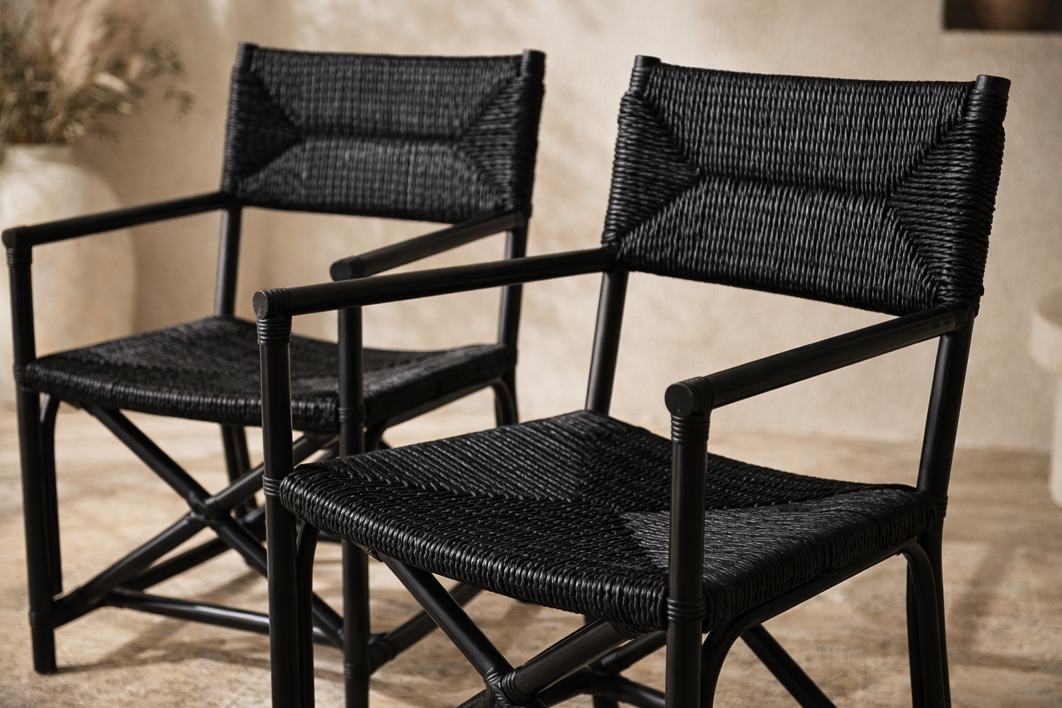 Saga black rattan dining chairs with woven seats and backs, styled as a pair in a warm neutral interior with textured plaster walls and soft natural light.