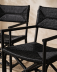 Saga black rattan dining chairs with woven seats and backs, styled as a pair in a warm neutral interior with textured plaster walls and soft natural light.