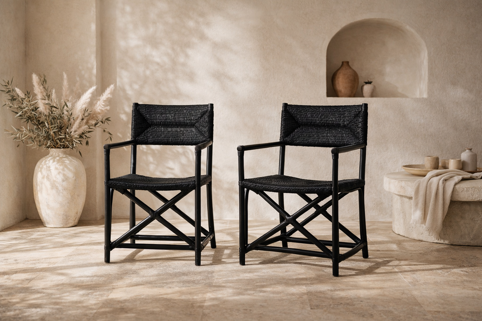 Saga black rattan dining chairs with woven seats and backs, styled as a pair in a warm neutral interior with textured plaster walls and soft natural light.