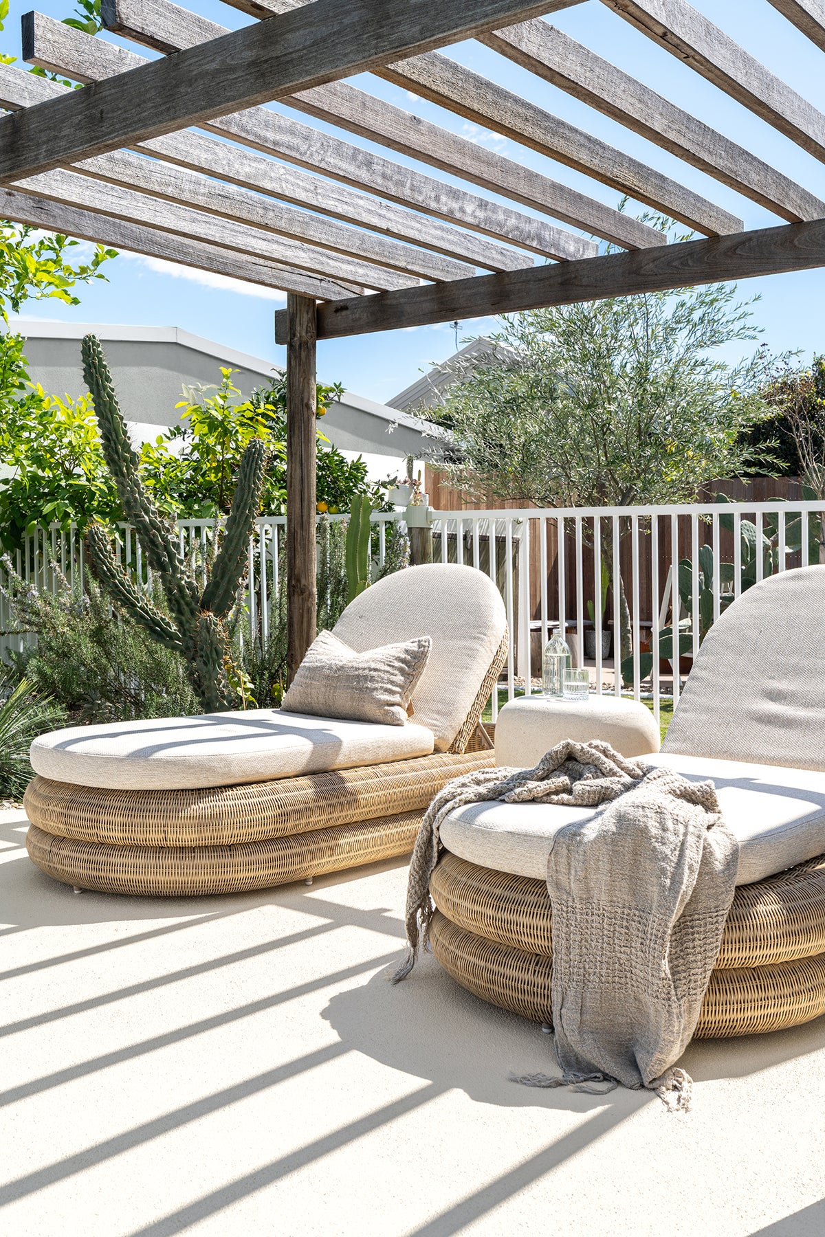 KULALA Living Sage Rectangle Cushion and Cairo Linen Throw styled on natural woven outdoor sun loungers beneath a timber pergola in a sunlit poolside setting.