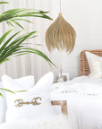 Coastal-inspired bedroom featuring a handwoven seagrass pendant light, rattan bed frame, and layered white linen styling