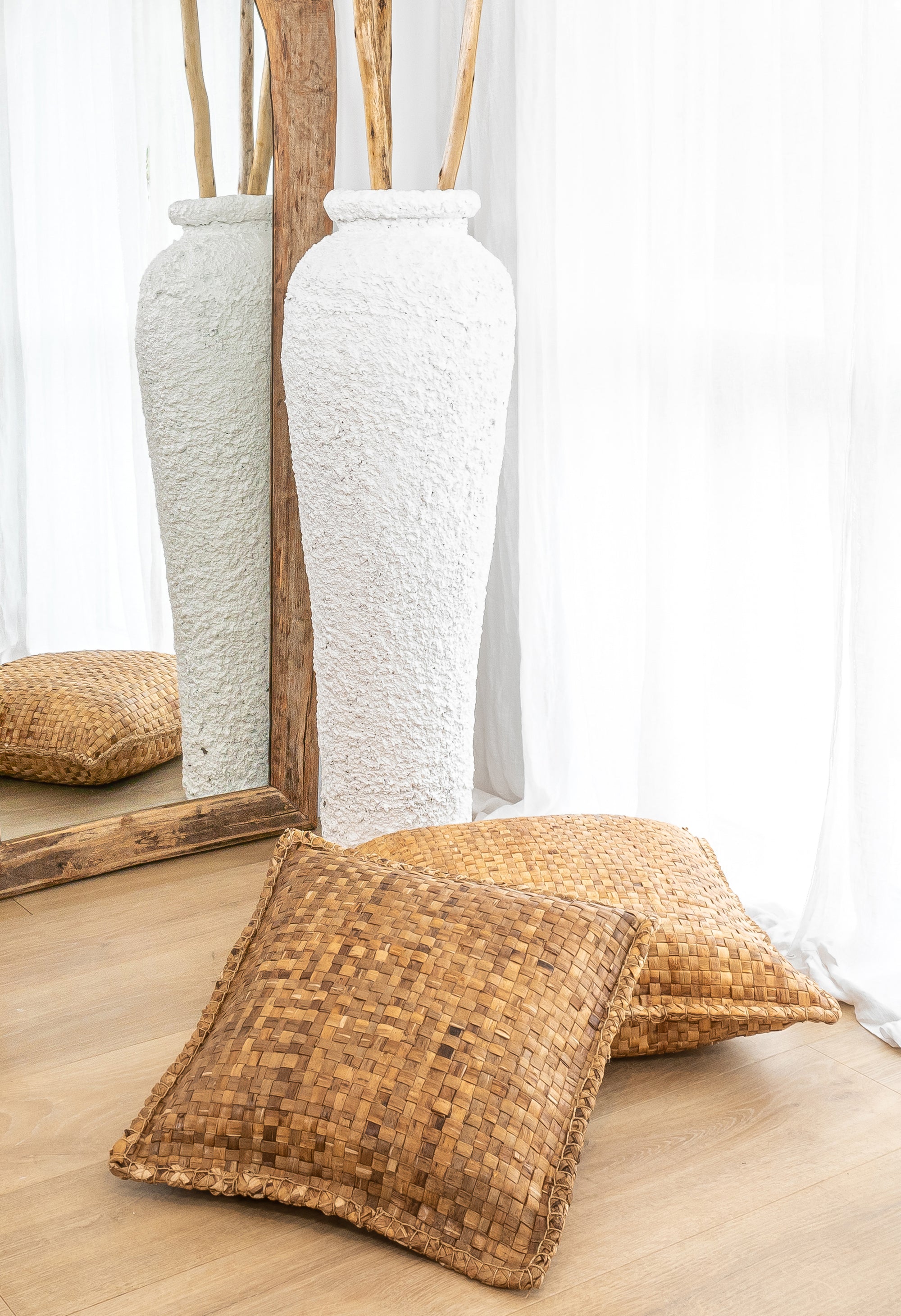 Seagrass floor cushions styled with a textured white vase and rustic wooden mirror, creating a natural and organic aesthetic in a serene space