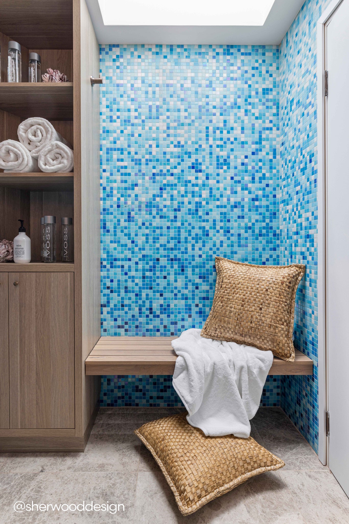 Seagrass cushions styled on a wooden spa bench with blue mosaic tiles, adding natural texture to a serene and luxurious wellness space