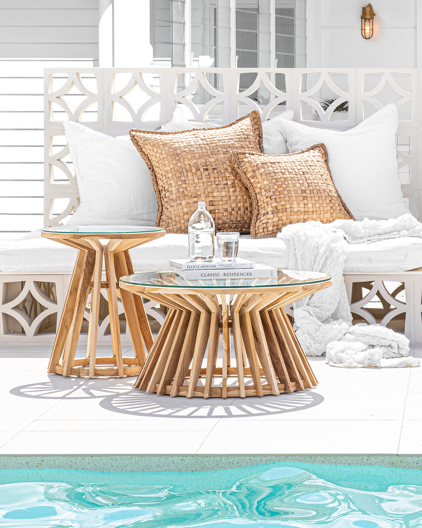 Seagrass cushions styled on a white outdoor lounge by the pool, complemented by teak and glass coffee tables, creating a serene and inviting coastal retreat