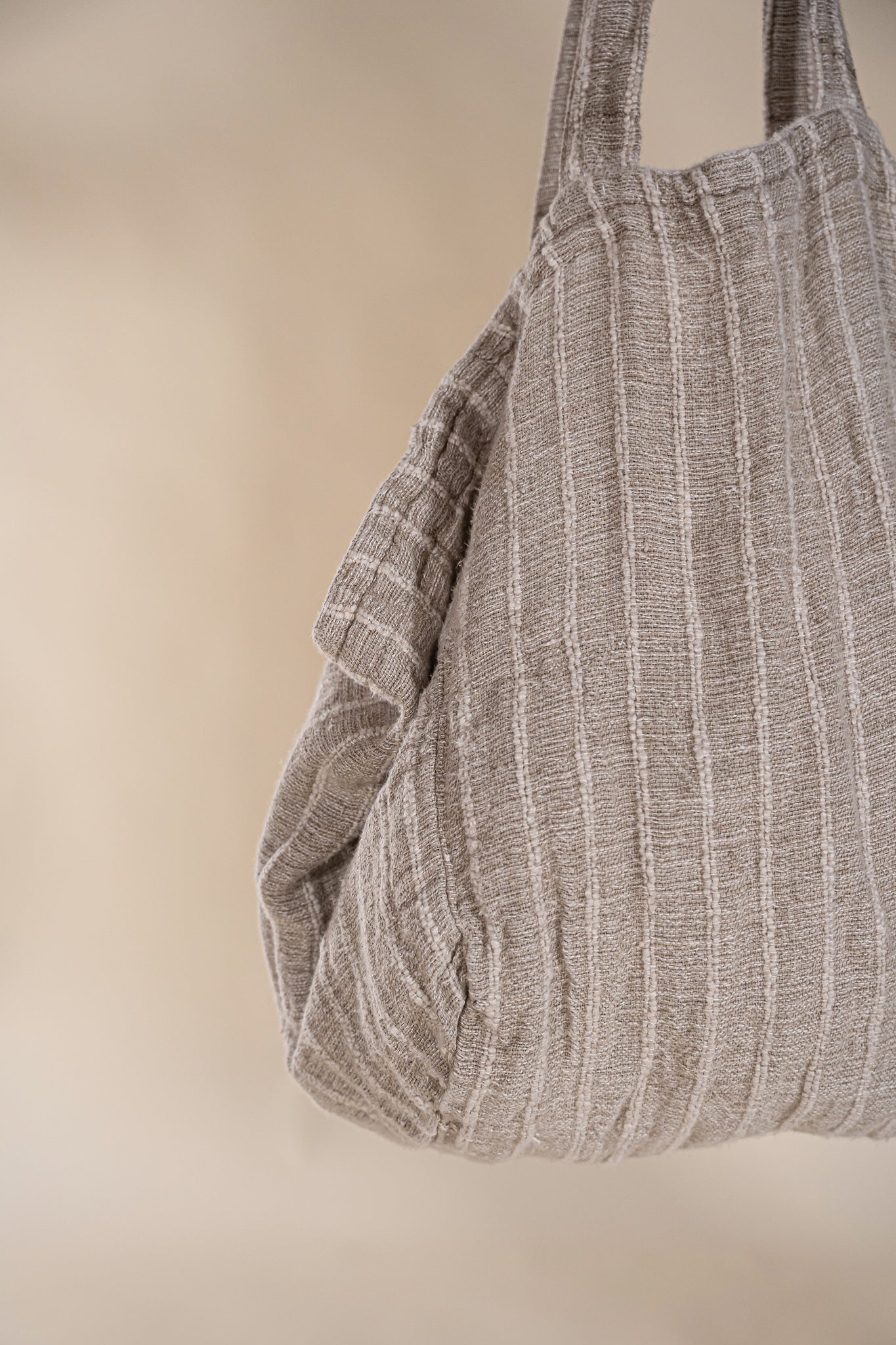 A generously sized striped linen market bag with a relaxed, slouchy design and exterior pocket. The neutral-toned fabric and soft texture create a timeless, effortless style
