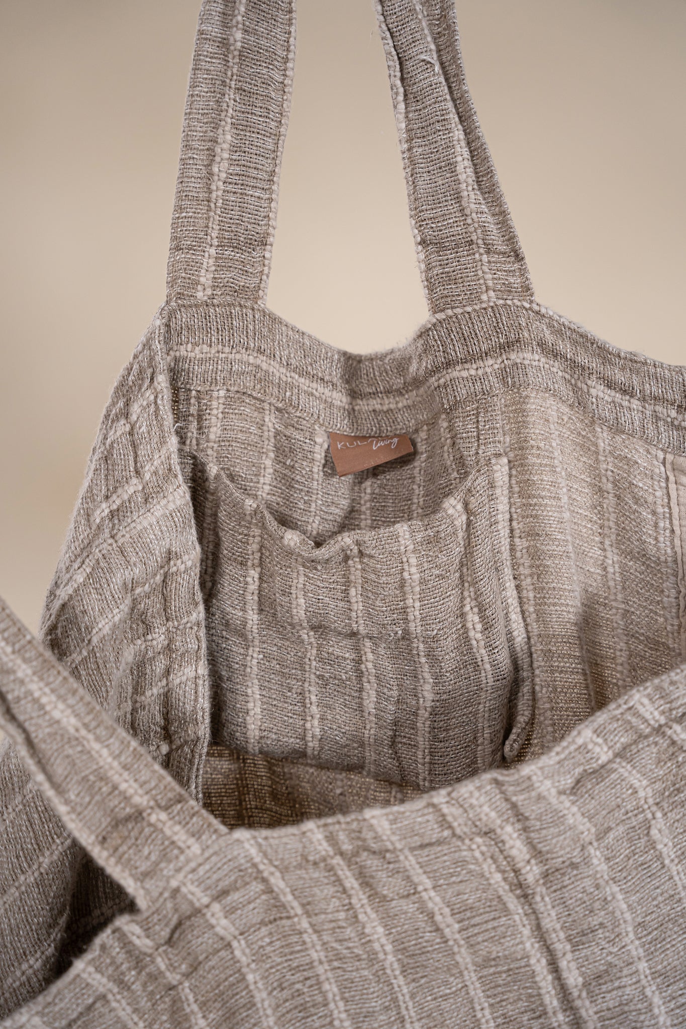 A generously sized striped linen market bag with a relaxed, slouchy design and exterior pocket. The neutral-toned fabric and soft texture create a timeless, effortless style