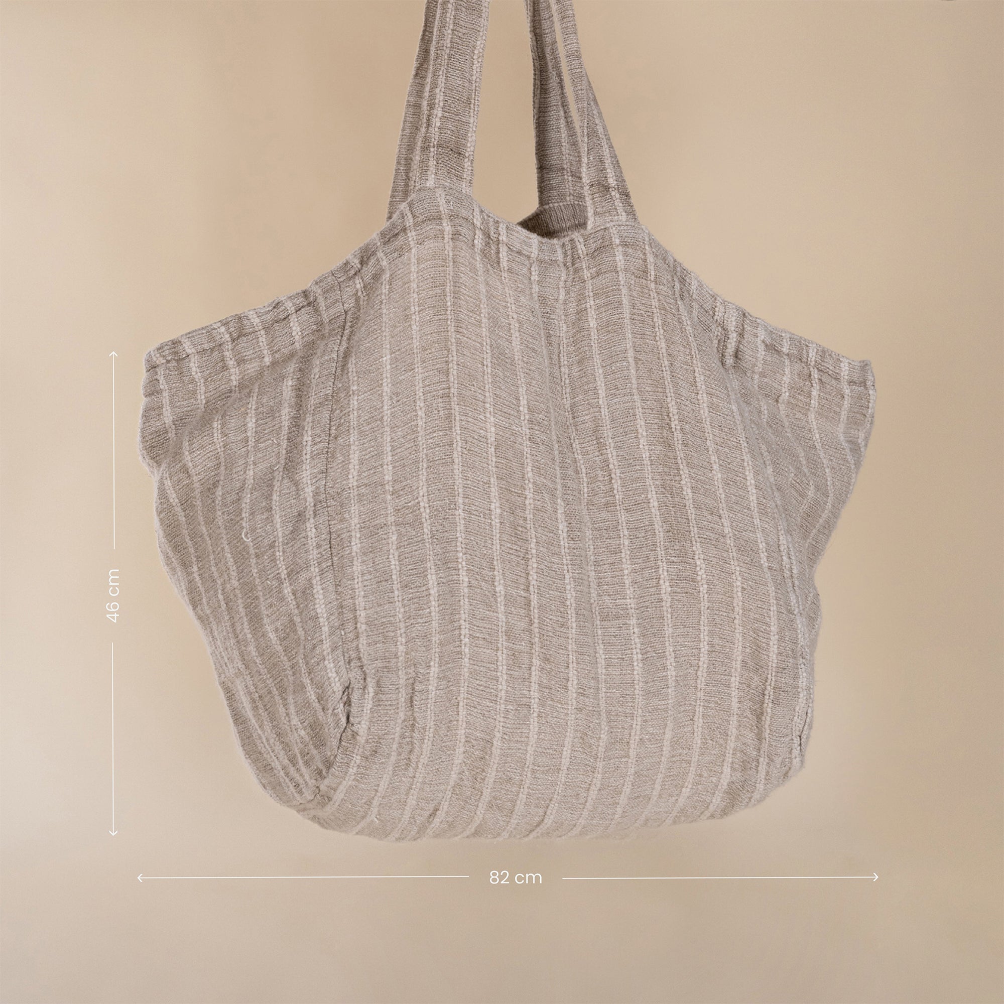 A generously sized striped linen market bag with a relaxed, slouchy design and exterior pocket. The neutral-toned fabric and soft texture create a timeless, effortless style