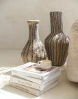 Pair of striped paper mache vases styled on a neutral surface, accompanied by books and a ceramic cup, creating a modern bohemian aesthetic.