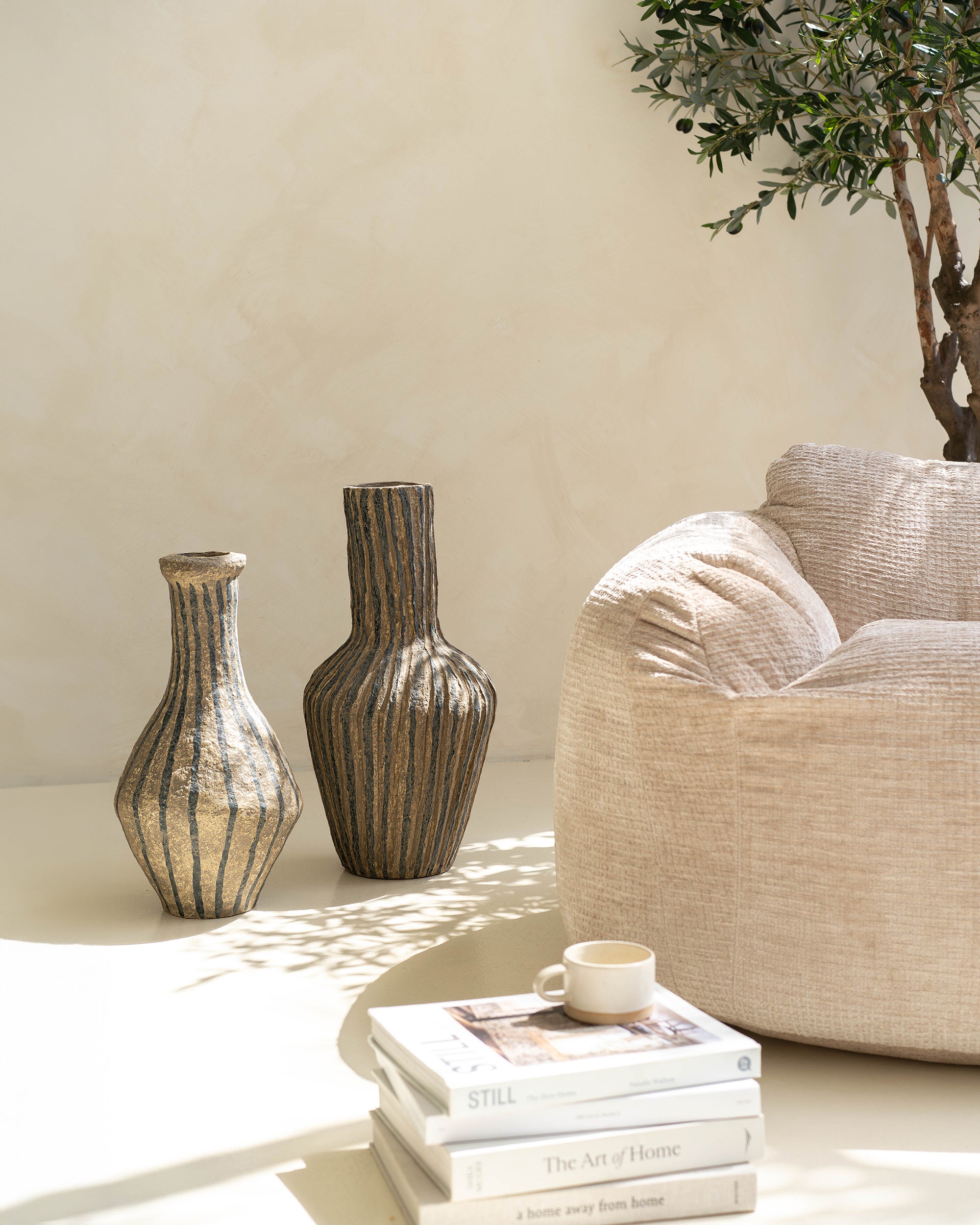Pair of striped paper mache vases styled on a neutral surface, accompanied by books and a ceramic cup, creating a modern bohemian aesthetic.
