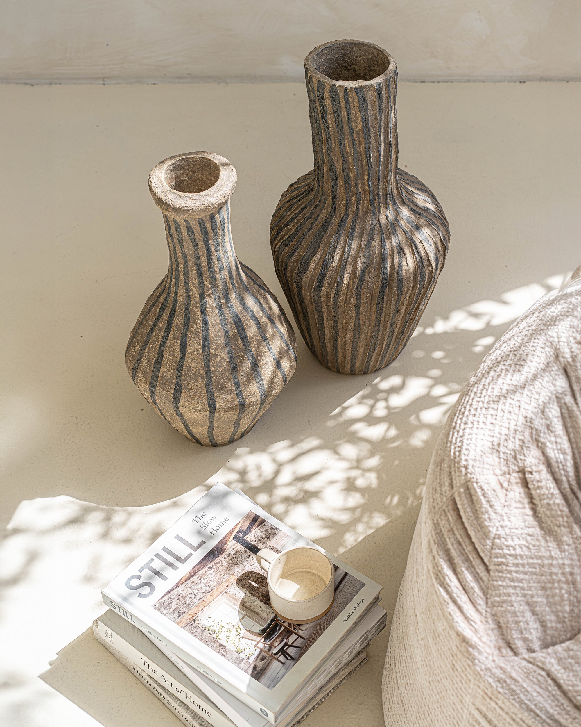 Pair of striped paper mache vases styled on a neutral surface, accompanied by books and a ceramic cup, creating a modern bohemian aesthetic.