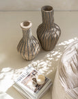 Pair of striped paper mache vases styled on a neutral surface, accompanied by books and a ceramic cup, creating a modern bohemian aesthetic.