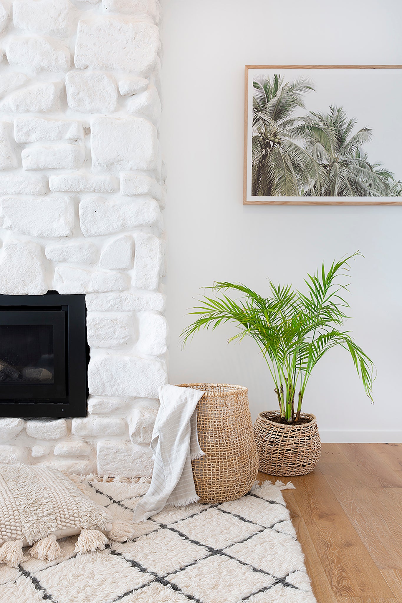 A beautifully styled corner featuring a woven natural fibre basket with a soft throw, a textured planter with lush greenery, and a white stone fireplace, creating a warm and inviting interior