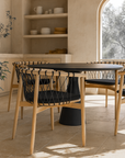 Sumbe Dining Chairs in black rope and natural teak wood styled around a black round table in a warm Mediterranean-inspired dining space with curved architectural details.