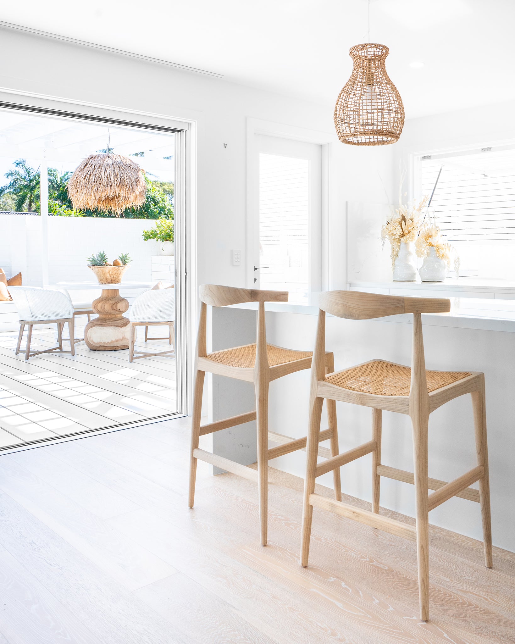 Scandinavian sungkai rattan bar stools with rattan seats, styled in a bright coastal kitchen with natural accents