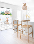 Scandinavian sungkai rattan bar stools with rattan seats, styled in a bright coastal kitchen with natural accents