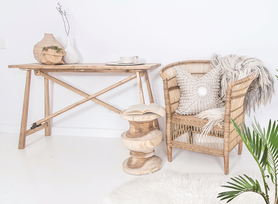 Tara teak console table styled with a natural rattan armchair, sculptural wooden stool and neutral decorative accents in a light, minimal interior.