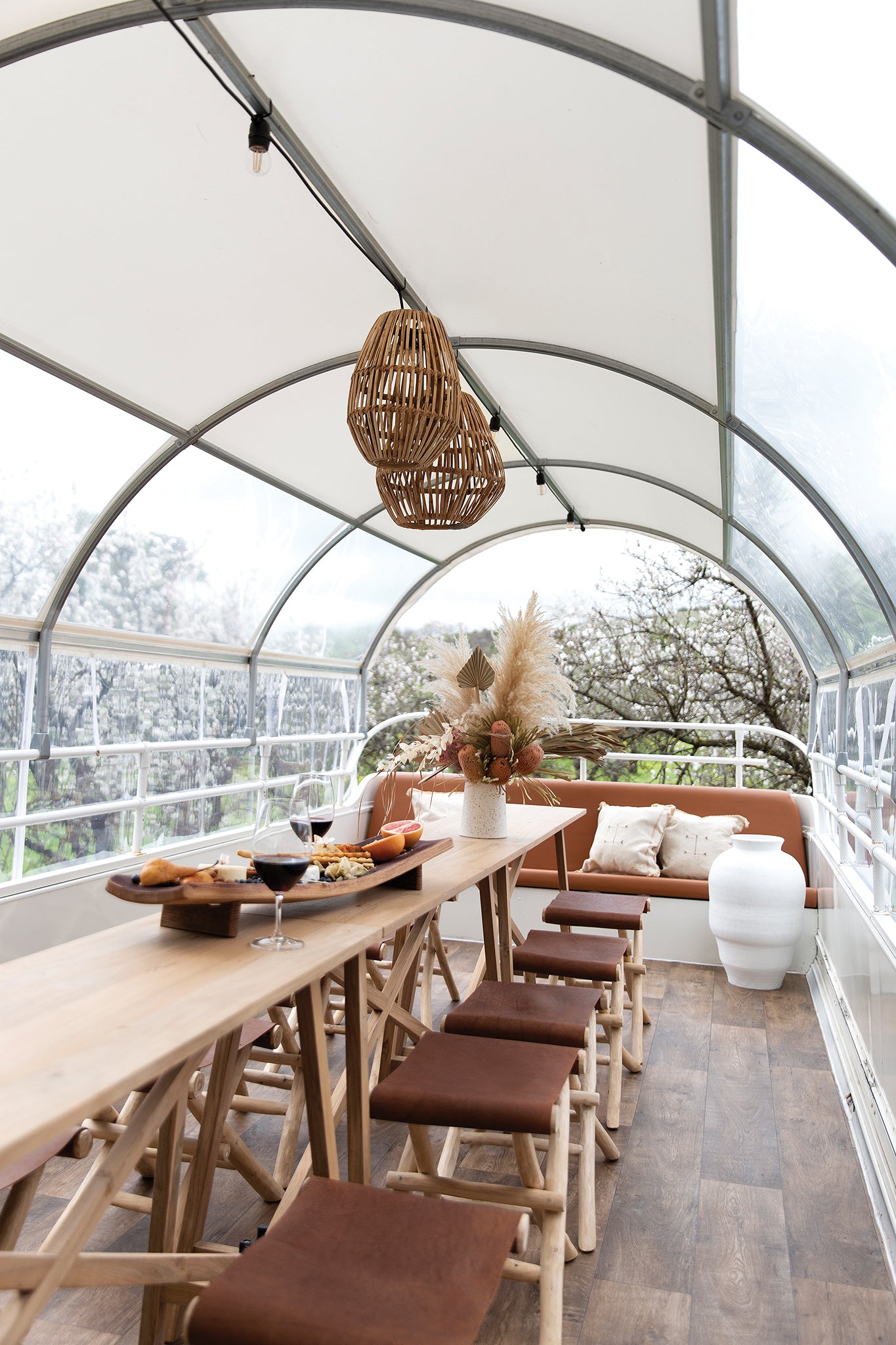 Tara teak console table styled in an outdoor dining setting with timber stools, leather seating, rattan pendant lights and a neutral floral arrangement.
