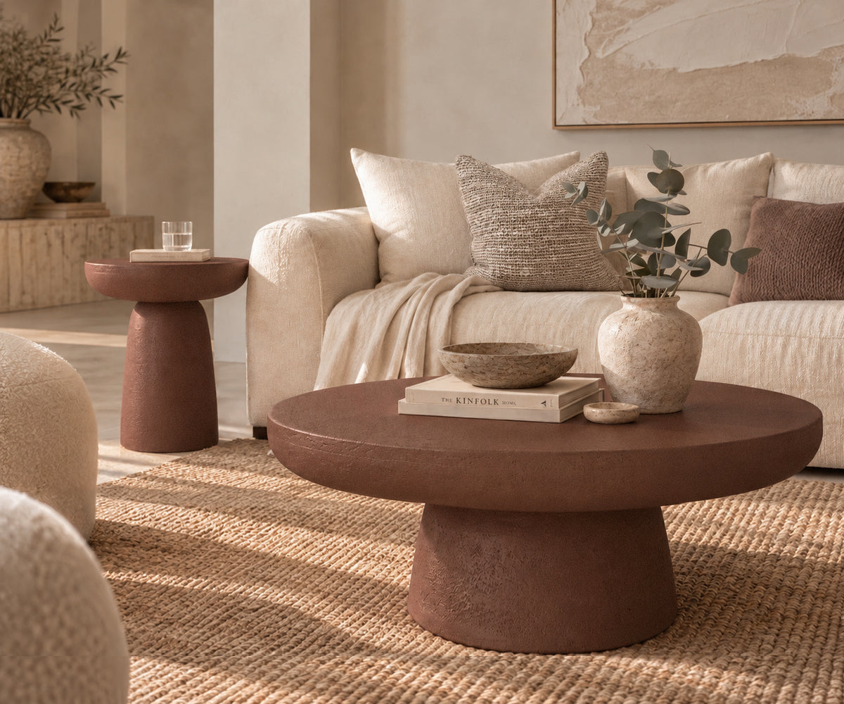 Tarran Coffee Table in Cinnabar Clay with a textured round top and sculptural base, styled with neutral décor beside a cream sofa on a woven rug.