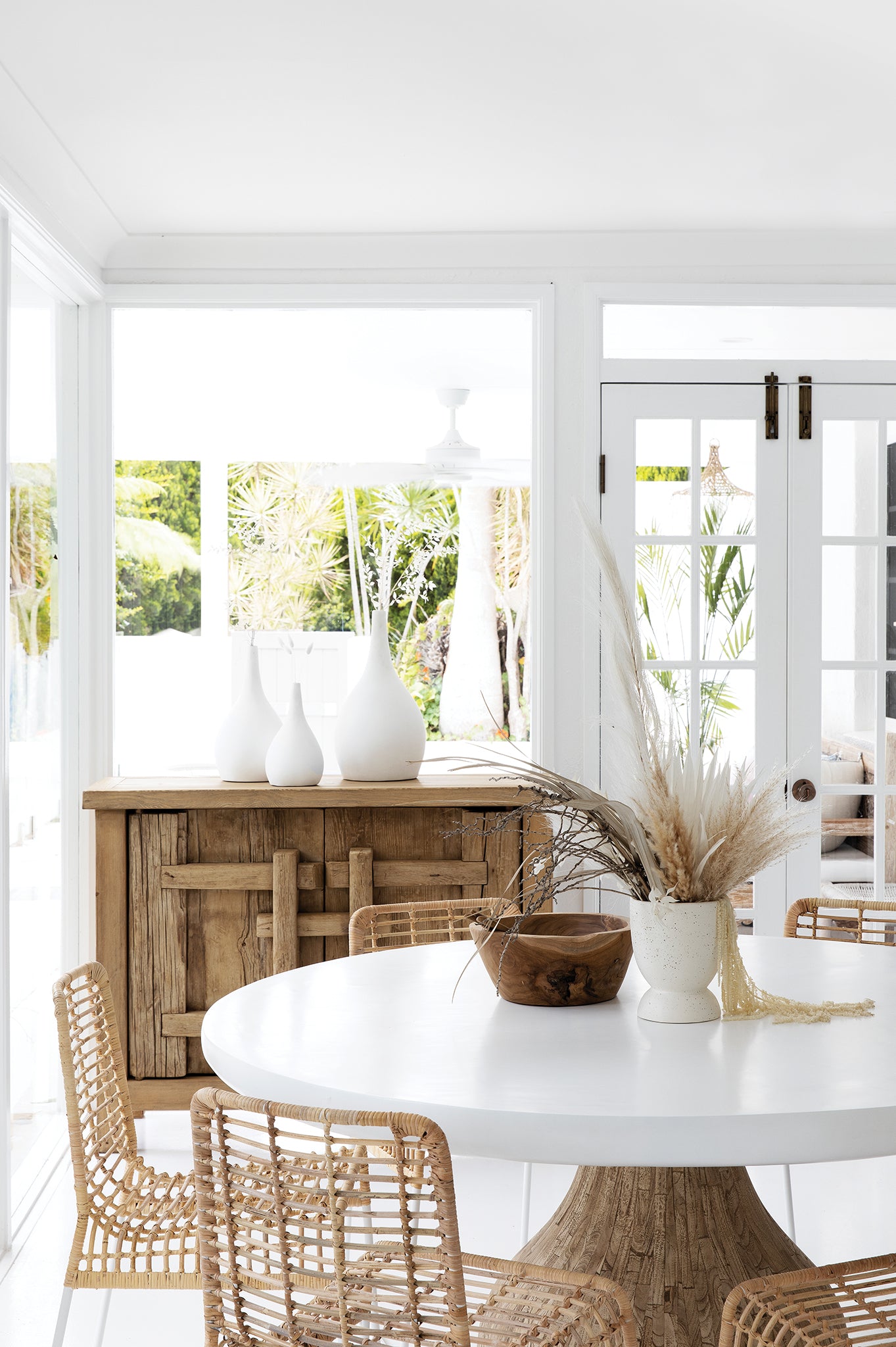 Natural warm brown teak carved bowl styled on a round white dining table with woven chairs, soft neutral decor and bright natural light streaming through windows.