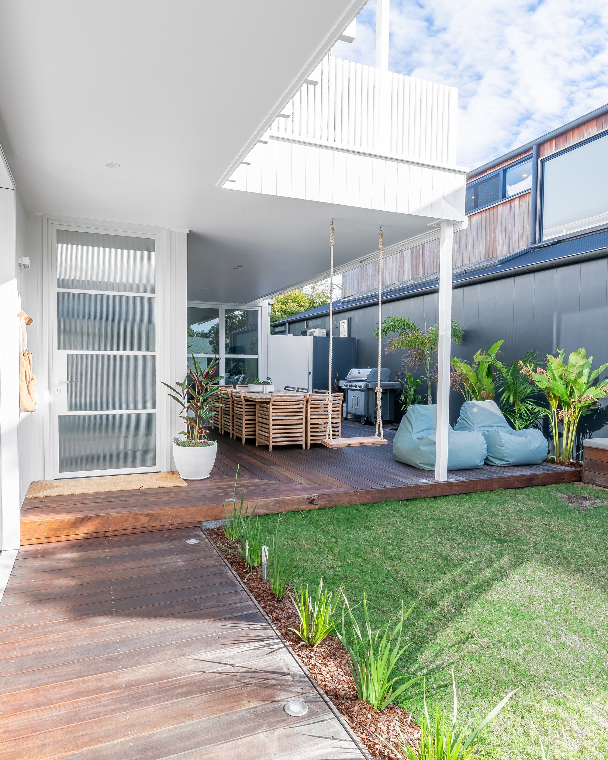 A spacious outdoor dining setting featuring a solid teak table and matching slatted dining chairs, designed for elegant alfresco entertaining on a timber deck