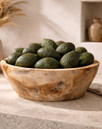 Large natural teak serving bowl filled with avocados, styled on a stone kitchen bench with neutral ceramics and olive oil in the background.
