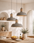 Terran fossil pendant cluster with textured stone finish and natural rope detail, suspended above a timber dining table in a warm neutral interior with woven chairs and soft daylight.