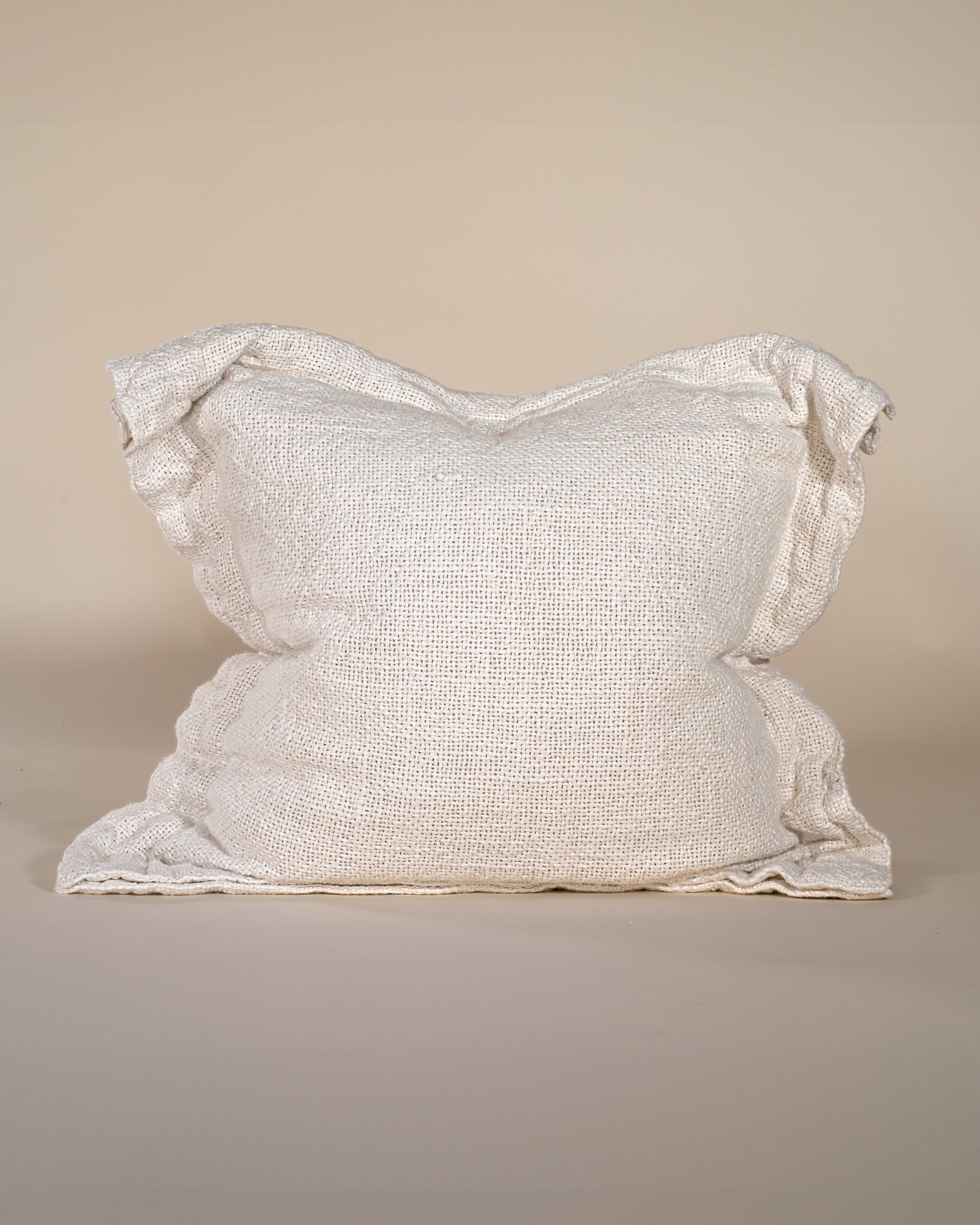 A textured linen cushion in a ivory tone, featuring a relaxed, oversized design with raw-edge detailing, set against a neutral backdrop