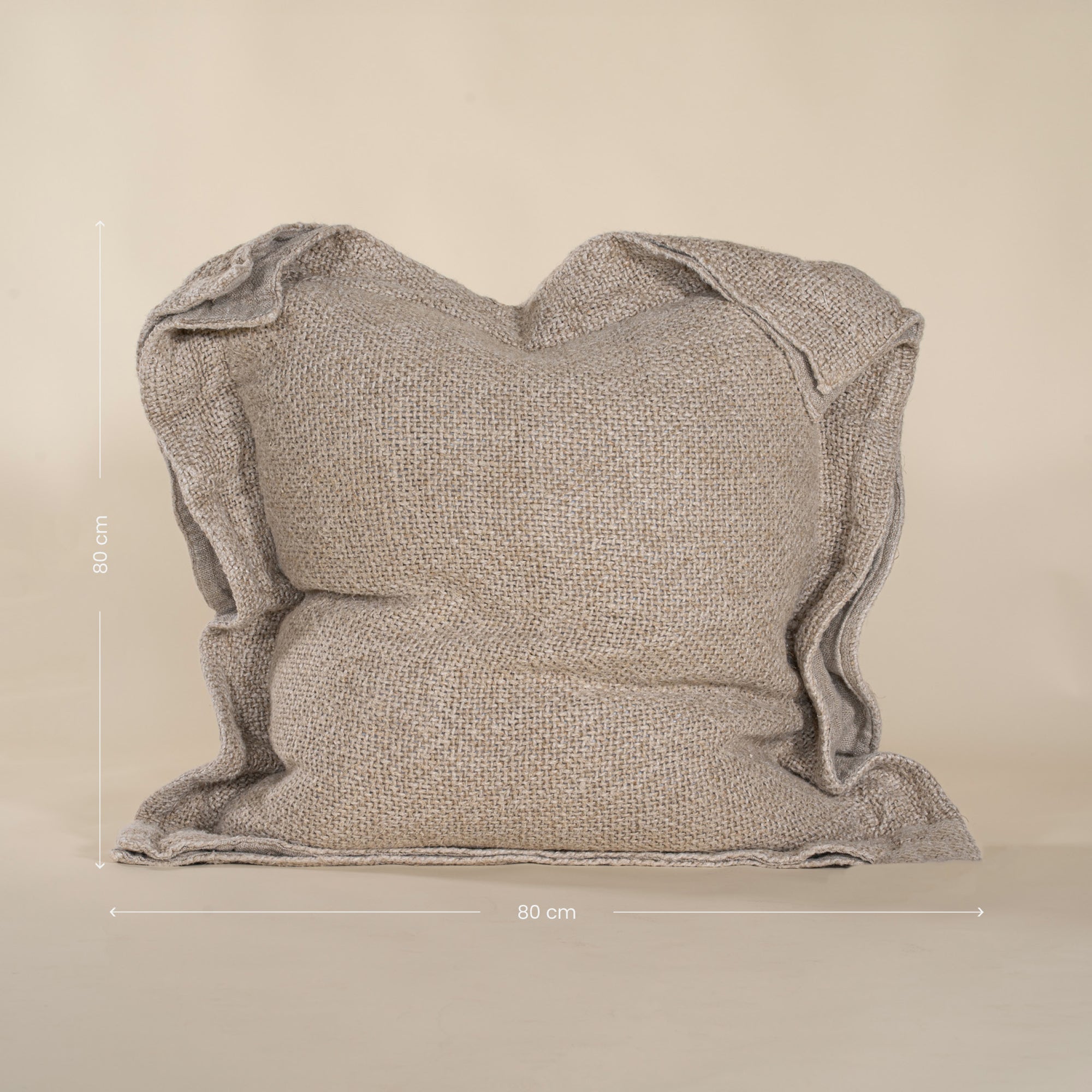 A textured linen cushion in a natural beige tone, featuring a relaxed, oversized design with raw-edge detailing, set against a neutral backdrop