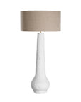 A textured paper mache white table lamp with elongated sculptural base and neutral linen shade, adding a refined and organic touch to any interior space