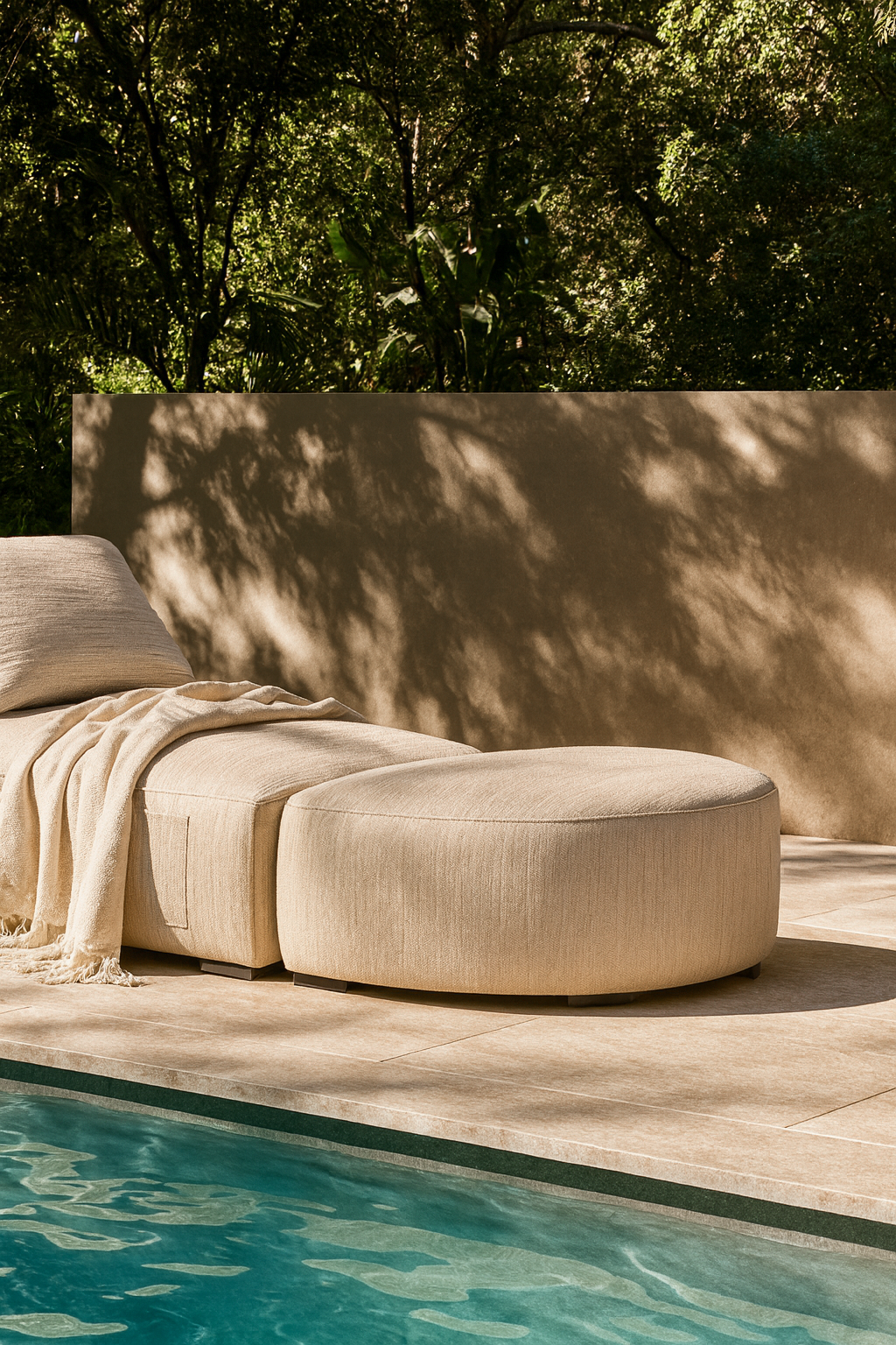 Travis Sofa and ottoman upholstered in natural fabric, styled with a throw blanket beside a swimming pool, creating a serene outdoor retreat