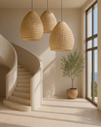 Three woven rattan pendant lights hanging above a curved stairwell in a coastal-inspired interior with natural light and potted olive tree