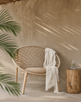 Tsonga Occasional Chair with handwoven seat and backrest, styled with a neutral throw in an outdoor patio setting with timber side table and natural textures.