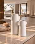 Umbono vase cluster in soft white textured finish with sculptural handles styled on a sunlit stone surface.