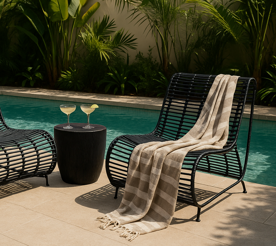 Villa Occasional Chairs in black styled beside a pool with a round kisiki side table, striped throw, and cocktails in a tropical outdoor setting