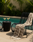 Villa Occasional Chairs in black styled beside a pool with a round kisiki side table, striped throw, and cocktails in a tropical outdoor setting