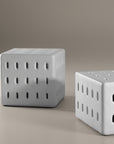 A modern white concrete table with perforated details, blending sculptural design with functional seating for indoor and outdoor spaces