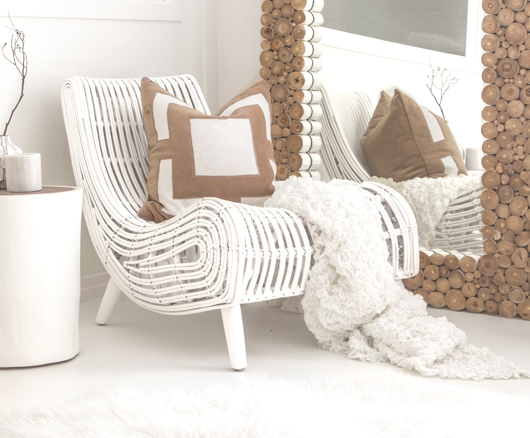 A stylish white rattan lounge chair with an organic, sculptural form, featuring a handwoven frame and elegant wooden legs. Styled with neutral cushions and a cosy throw, creating a relaxed and inviting living space
