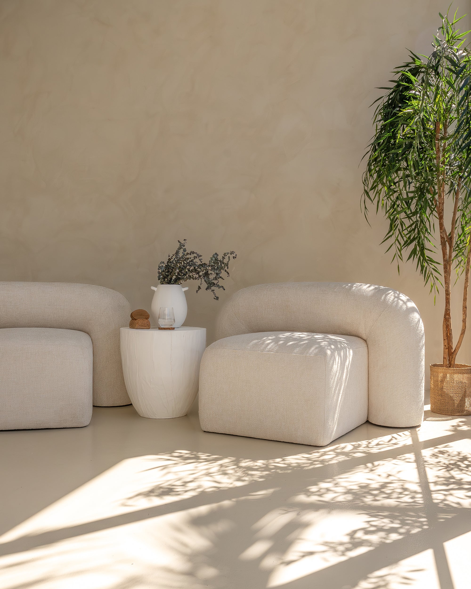 Modern white magnesium oxide side table styled with a ceramic vase and dried florals, complementing a neutral-toned curved sofa