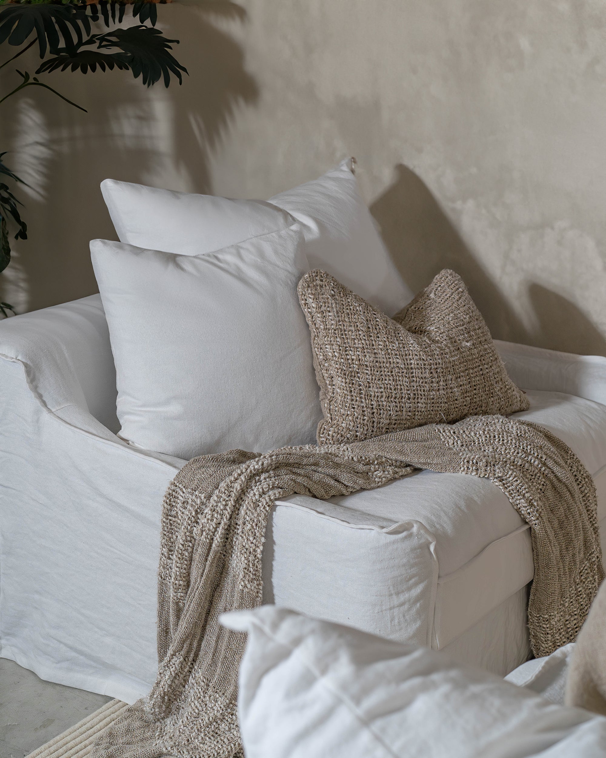 White linen one seater sofa styled with neutral textured cushions and a knitted throw in a minimalist living room setting