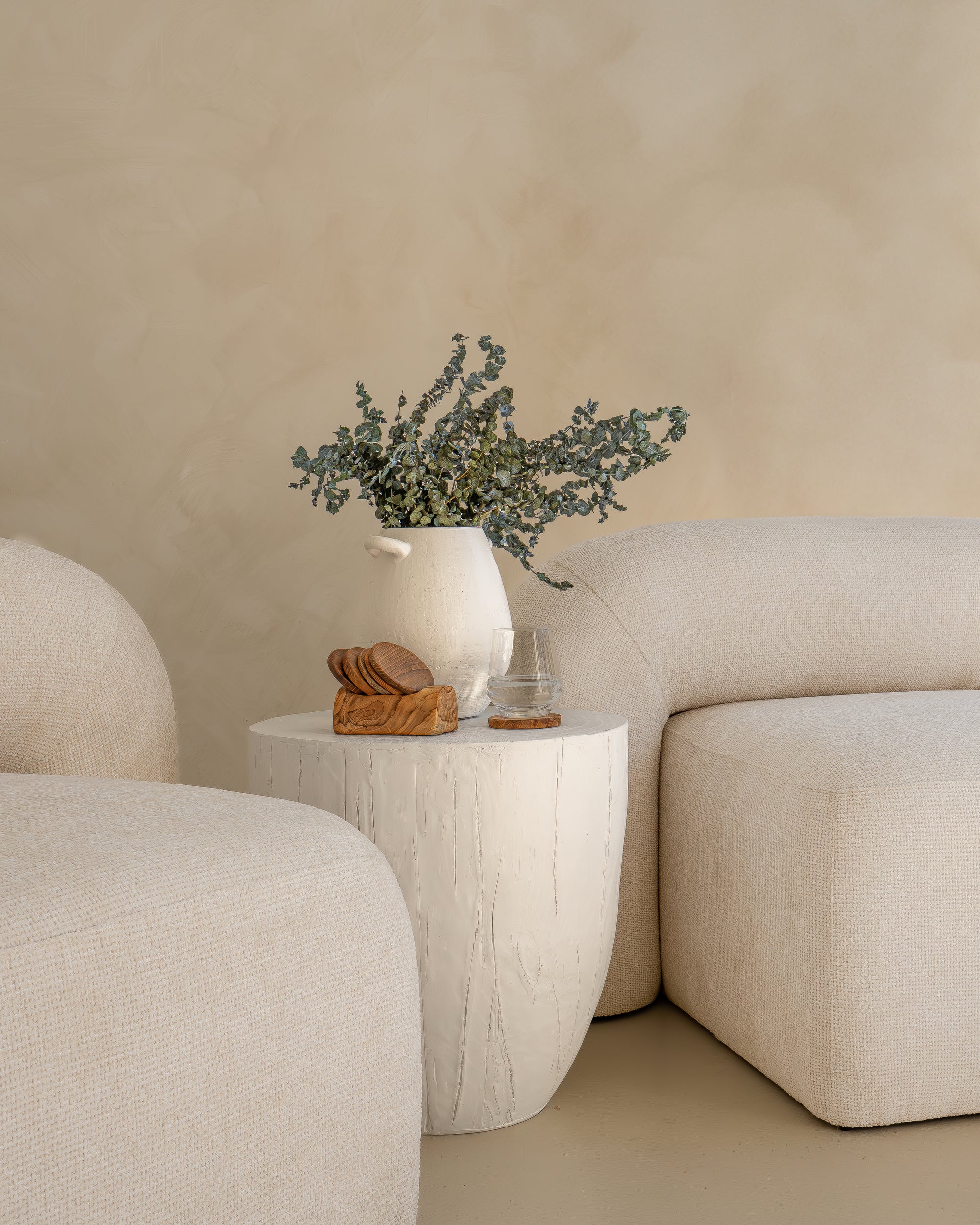 Modern white magnesium oxide side table styled with a ceramic vase and dried florals, complementing a neutral-toned curved sofa