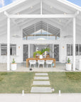 A beautifully designed coastal outdoor living space featuring a spacious dining area, white woven lounge seating, and natural wood accents, perfect for relaxed alfresco entertaining
