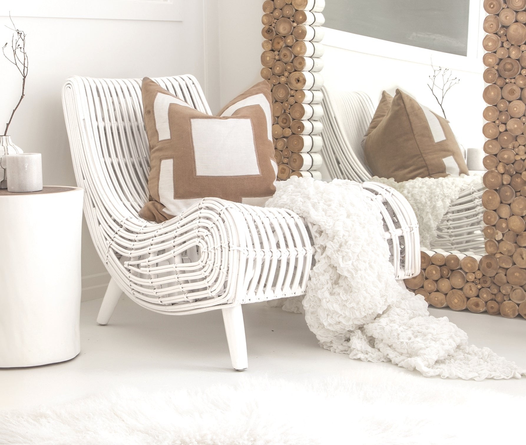A stylish white rattan lounge chair with an organic, sculptural form, featuring a handwoven frame and elegant wooden legs. Styled with neutral cushions and a cosy throw, creating a relaxed and inviting living space