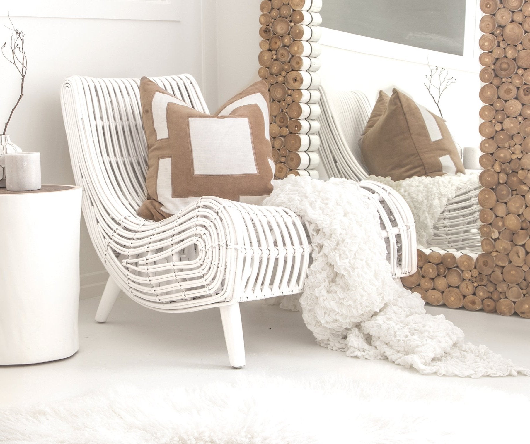 A stylish white rattan lounge chair with an organic, sculptural form, featuring a handwoven frame and elegant wooden legs. Styled with neutral cushions and a cosy throw, creating a relaxed and inviting living space