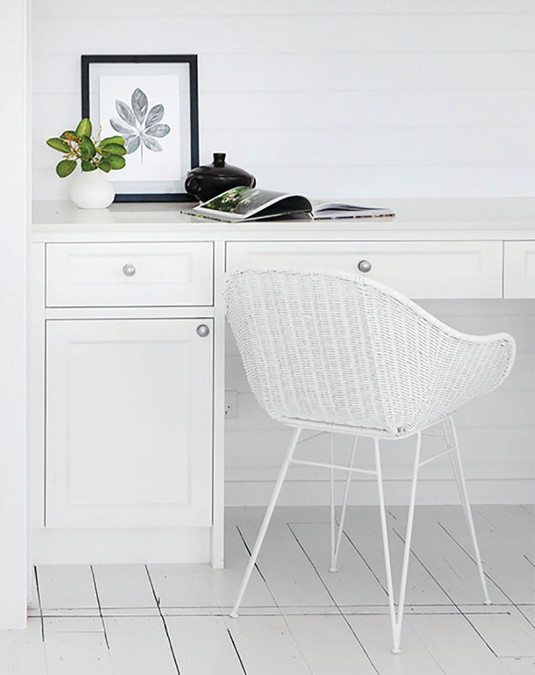 Coastal home office with white rattan desk chair and minimal decor, featuring natural elements and crisp white cabinetry